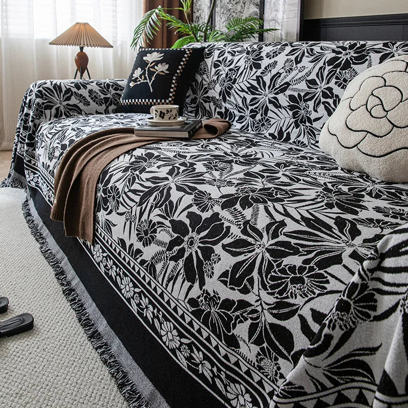 A black and white floral jacquard sofa throw blanket draped over a sofa with natural light.
