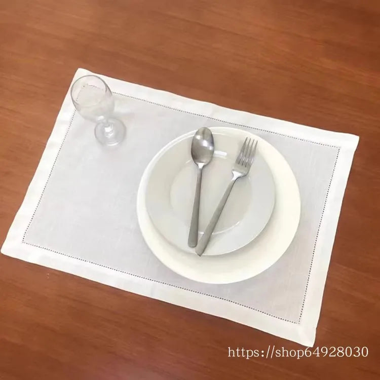 A white plate with a spoon and fork is placed on a white linen napkin on a wooden table.