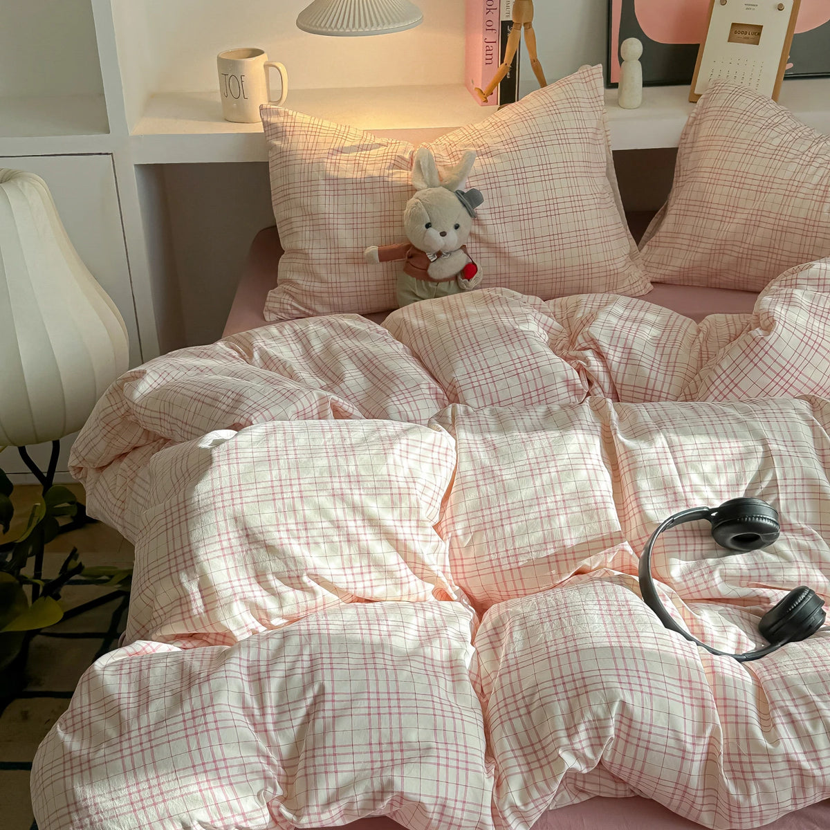 A pink plaid duvet cover set with matching pillowcases and a small stuffed rabbit toy on a bed.