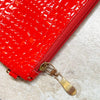 Close-up of a red crocodile embossed fabric bag with a gold metal zipper pull.