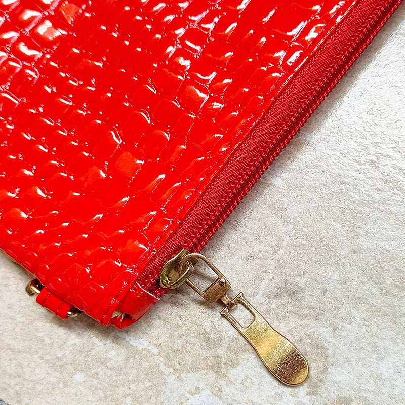 Close-up of a red crocodile embossed fabric bag with a gold metal zipper pull.