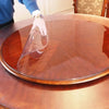 A hand is pouring clear liquid into a round waterproof PVC tablecloth on a wooden table.