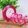 Pink satin ribbon rolled on a spool with white filler visible on a wooden surface