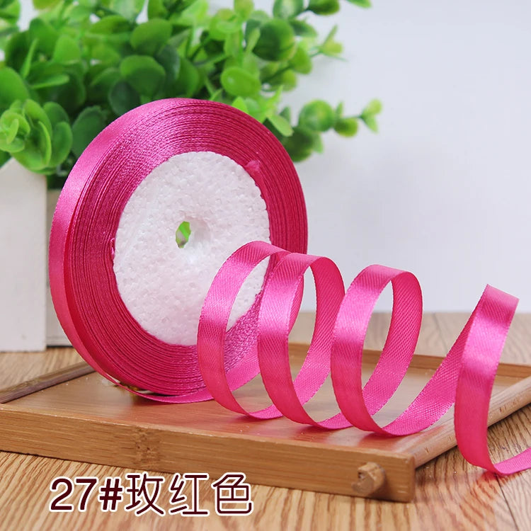 Pink satin ribbon rolled on a spool with white filler visible on a wooden surface