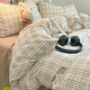 A plaid duvet cover set in beige and white checks with a fluffy rabbit pillow visible on the bed.