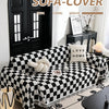 A black and white checkerboard sofa slipcover displayed on a couch with a dark door in a bright room.