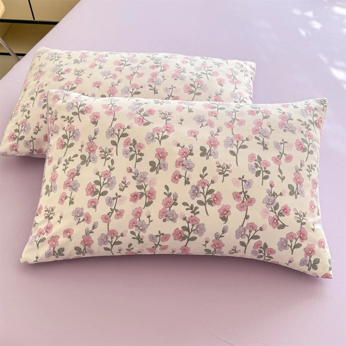 A light pink floral printed pillow cover resting on a purple surface.