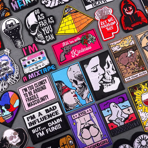 A collection of dark and colorful iron-on embroidery patches featuring skulls, guns, text, and abstract designs.