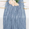 A blue cheesecloth table runner with a textured, wrinkled appearance, featuring pink flowers and gold cutlery.