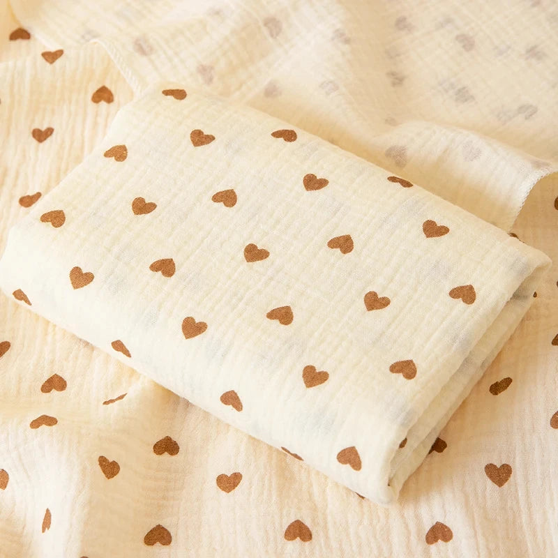 A rolled soft double-layer cotton baby swaddle blanket with small brown hearts on a light cream background.