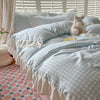 A light blue and white gingham duvet cover set with ruffled edges and a teddy bear toy on a bed.