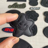 A hand holds a black embroidered leather star patch against a background of other similar patches.