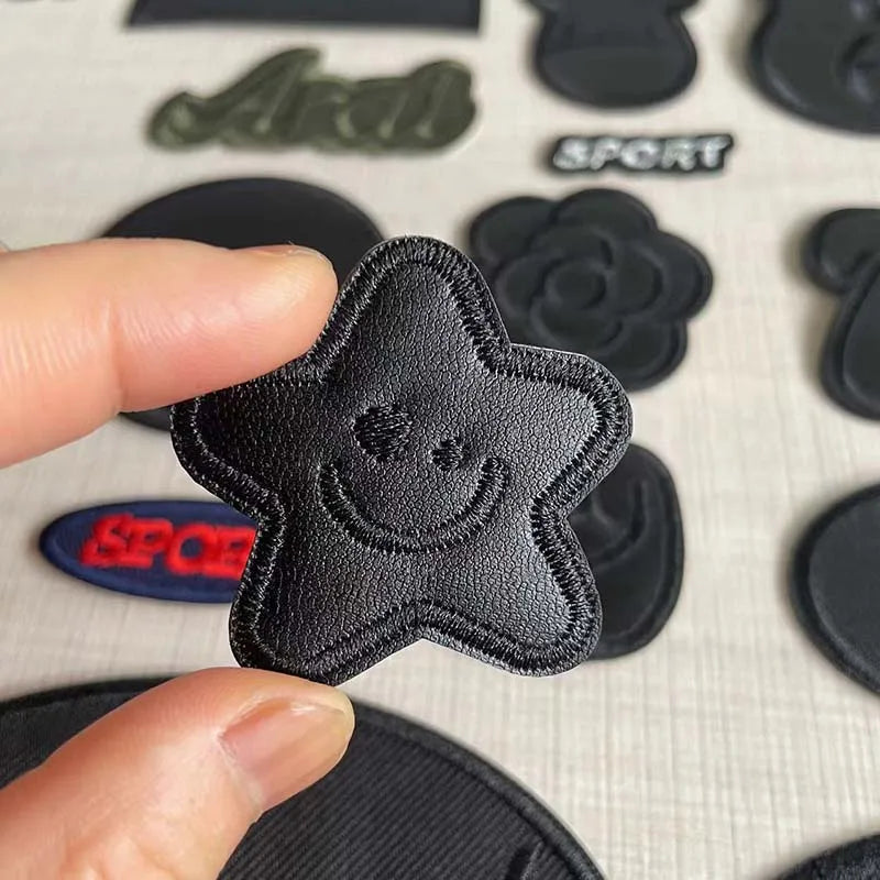 A hand holds a black embroidered leather star patch against a background of other similar patches.