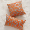 An orange and gray geometric patterned throw pillow resting on a white textured surface.