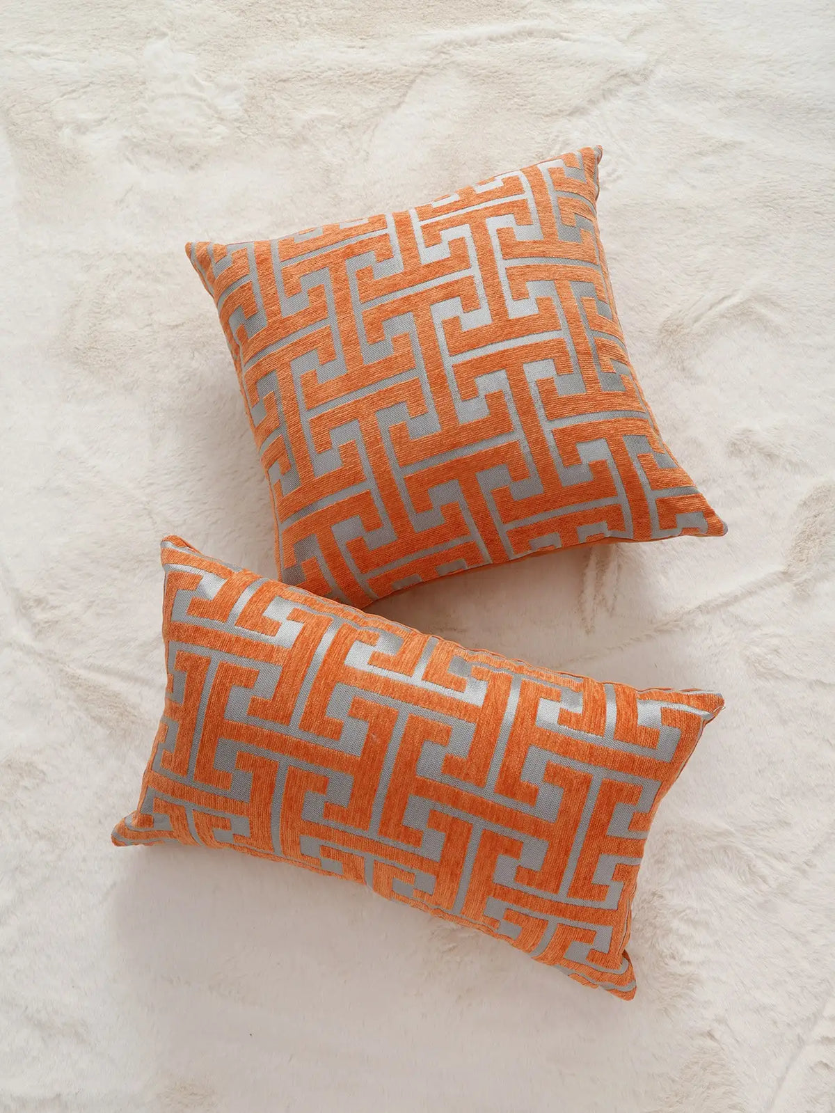 An orange and gray geometric patterned throw pillow resting on a white textured surface.