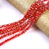 A strand of faceted, reddish-orange glass beads is unwrapped and laid out on a gold-colored fabric.