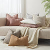 A collection of textured boucle throw pillows in shades of pink, beige, and gray arranged on a light-colored sofa.