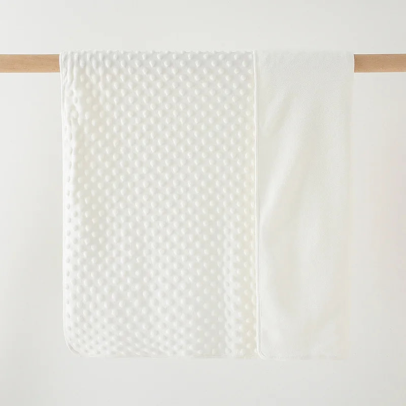 A white fleece throw blanket with a dimpled texture is hanging on a wooden rod.