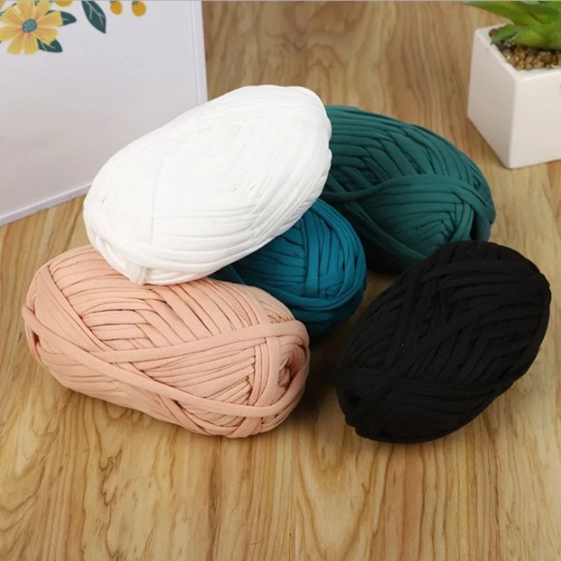A collection of thick polyester craft yarn in white, teal, pink, and black coiled on a wooden surface.