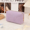 A lavender knitted cosmetic storage pouch with a gold zipper lies on a white textured surface.