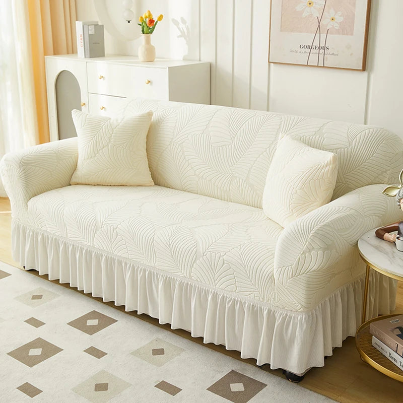 A cream jacquard elastic sofa cover with a ruffled skirt displayed in a bright room.
