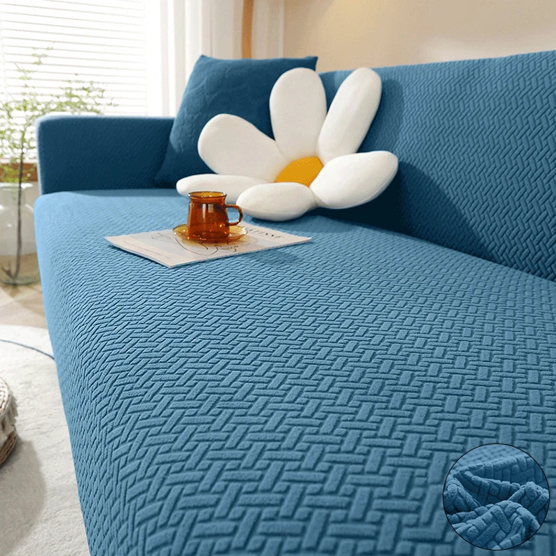 A teal jacquard sofa cover featuring a textured fabric and a white flower cushion with an orange accent.