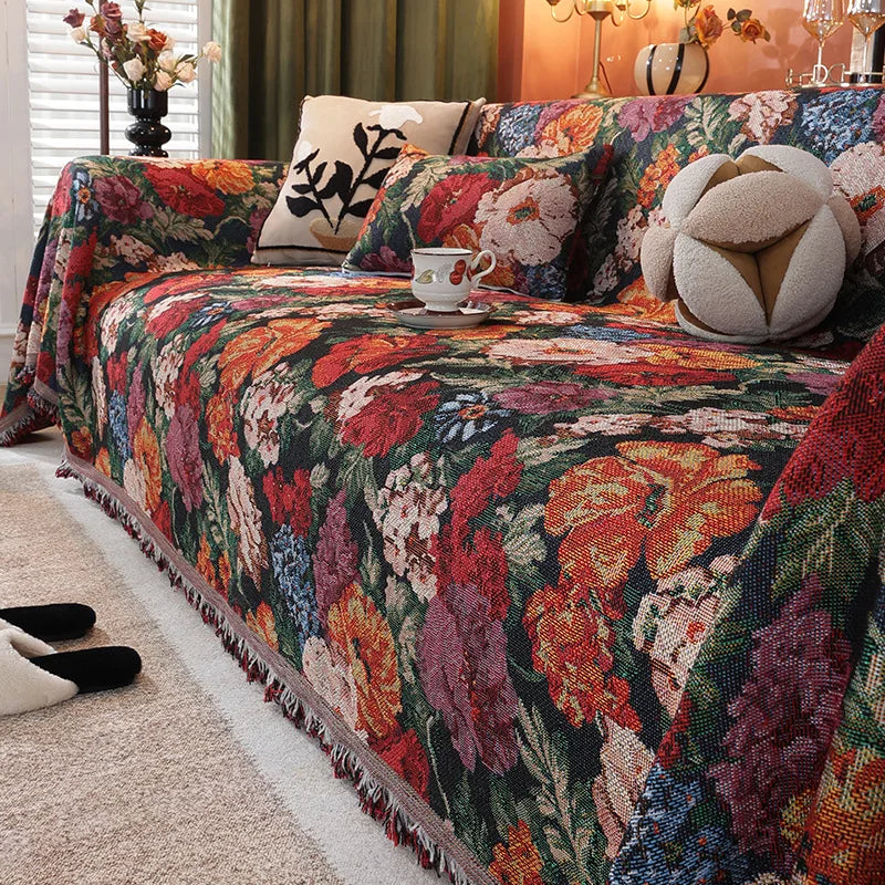 A richly patterned floral jacquard sofa throw blanket draped over a sofa with green curtains and decorative pillows.