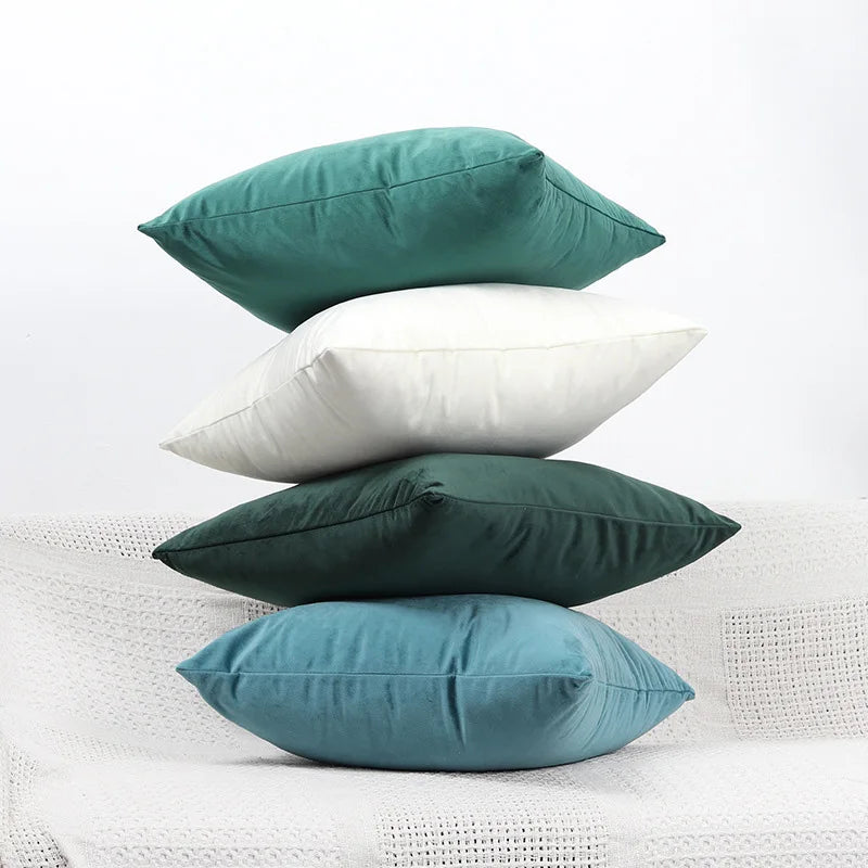Three velvet cushions in shades of teal, white, and dark green resting on a white textured surface.