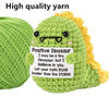 Handmade plush dinosaur toy made from green and yellow yarn with a positive dinosaur sign
