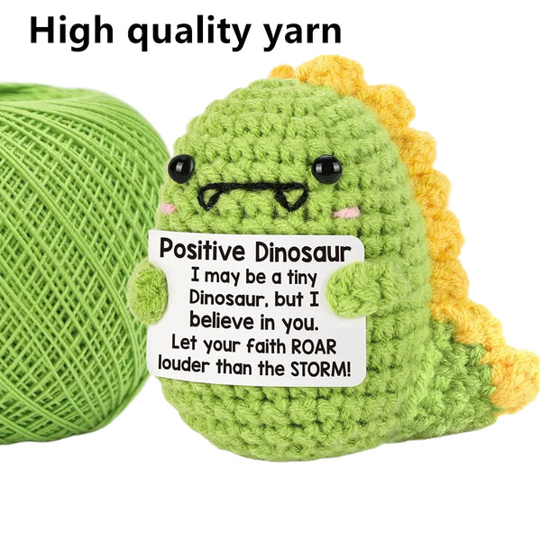Handmade plush dinosaur toy made from green and yellow yarn with a positive dinosaur sign