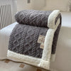 A thick gray fleece blanket with white trim is folded on a white bed, showing a diamond quilted pattern.