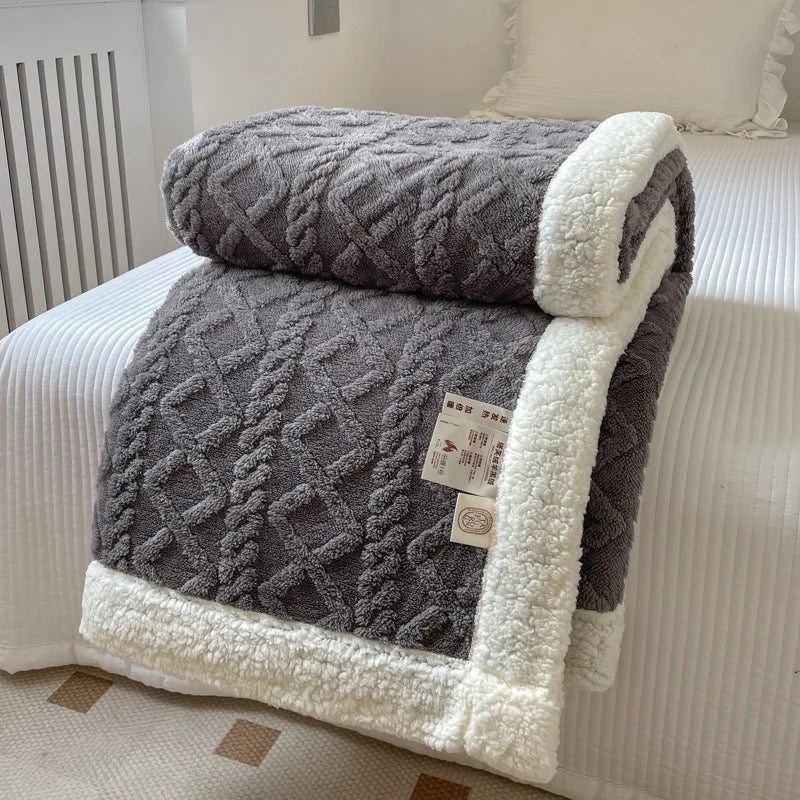 A thick gray fleece blanket with white trim is folded on a white bed, showing a diamond quilted pattern.