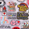 A collection of embroidered letter iron-on patches featuring various phrases like Book Lover Satan Loves Me and See The Good