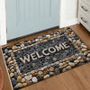 A rectangular welcome doormat with a dark gray background and light-colored stones, featuring the word WELCOME.