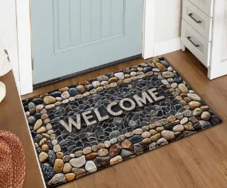 A rectangular welcome doormat with a dark gray background and light-colored stones, featuring the word WELCOME.