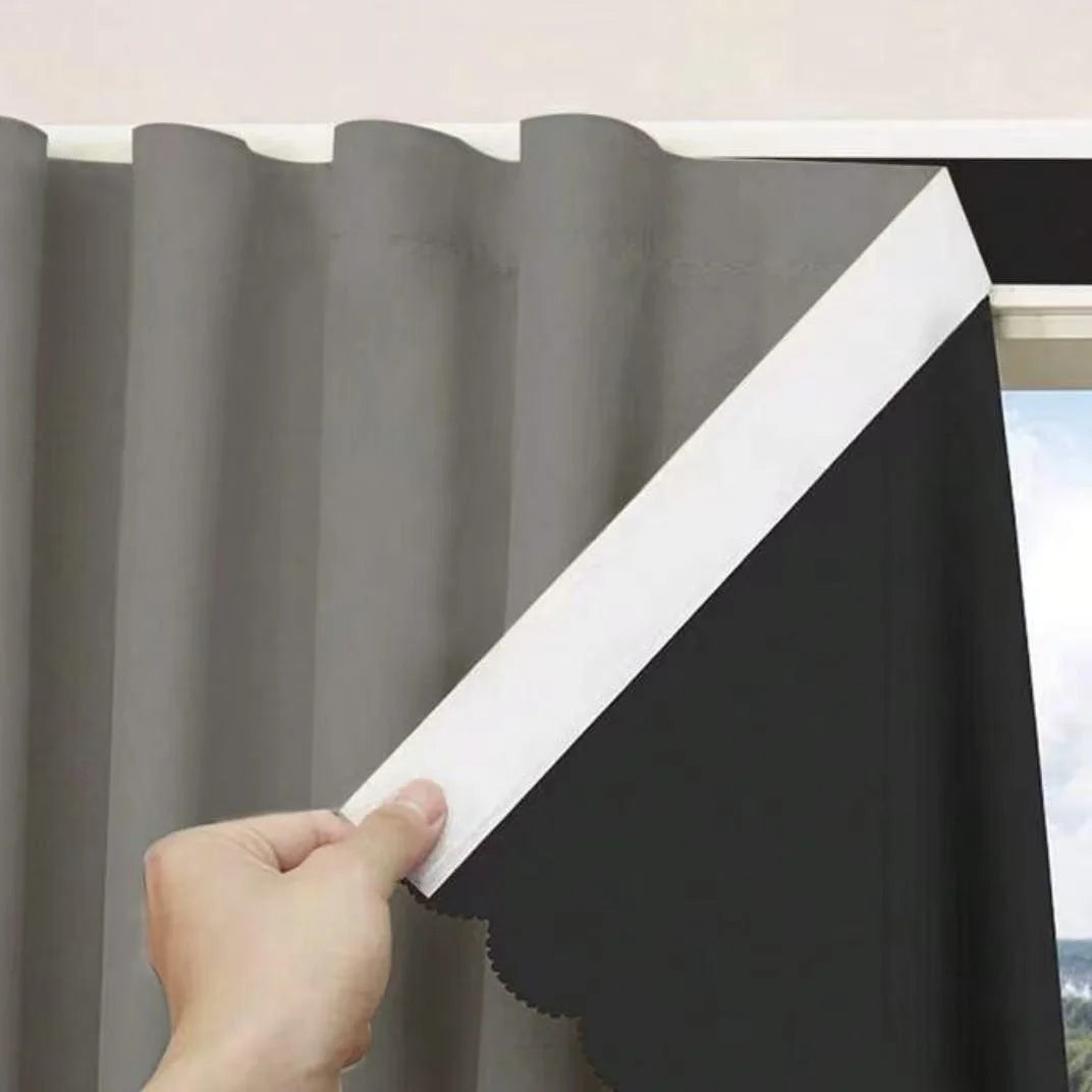 A hand is pulling a white blackout curtain panel across a gray curtain fabric.