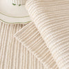 A close-up of a beige ribbed chenille cushion cover resting on a light rug next to a white ceramic dish.