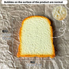A slice of toast is shown on brown paper, with bubbles on the surface and a small white sphere nearby.