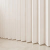 A close-up of a light beige, pleated fabric room divider curtain against a white wall.