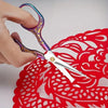 A hand holds a pair of vintage stainless steel sewing scissors against a red lace background.