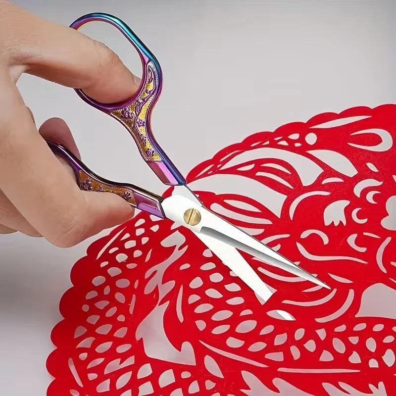 A hand holds a pair of vintage stainless steel sewing scissors against a red lace background.