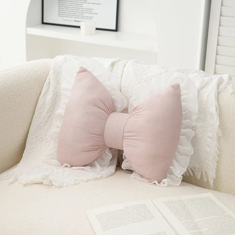 A pink embroidered sofa cushion with a lace trim is displayed on a light-colored sofa.