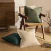 A set of linen fringe throw pillow covers in olive green and cream resting on a beige rug.