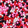 A close-up view of numerous imitation pearl beads in various shades of pink, red, white, and black.