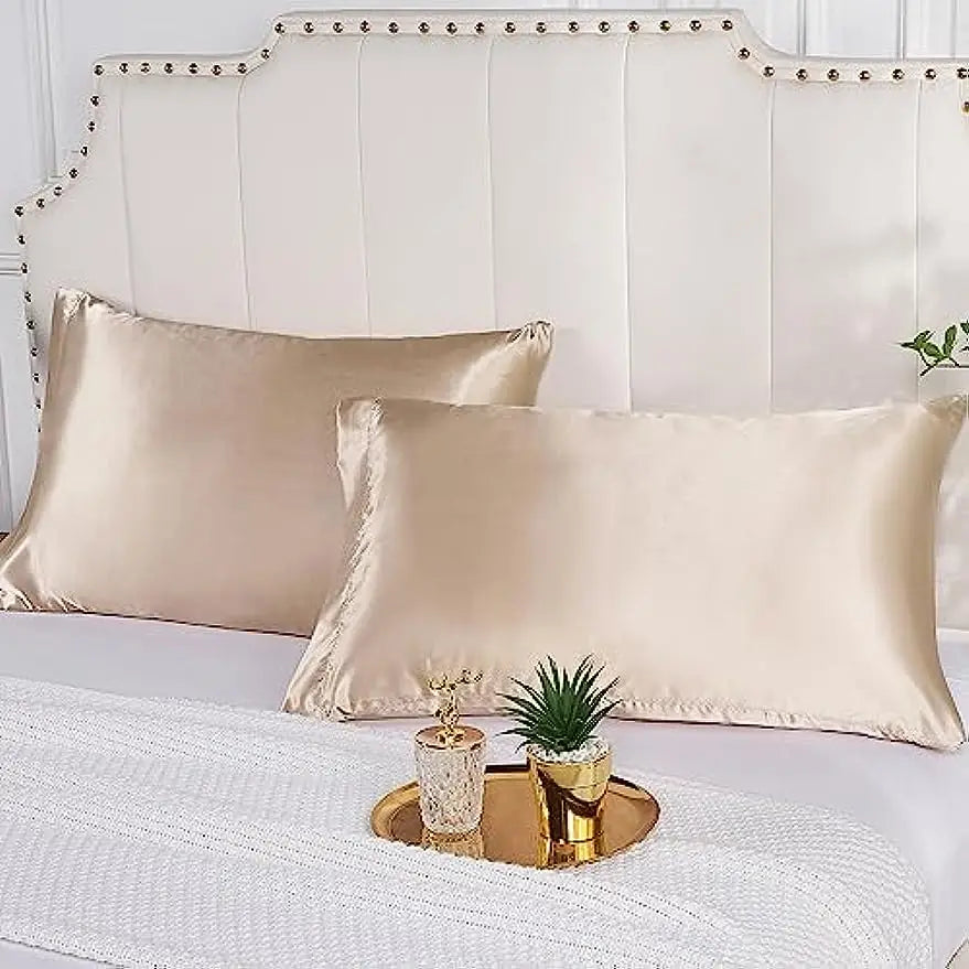 A set of silky satin pillowcases in champagne color displayed on a white surface.