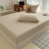 A fitted bed sheet cover is displayed on a white bed, next to a wooden shelf with books and a stuffed animal.