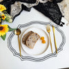 A white plate with sliced bread and gold cutlery is set on a black embroidered linen placemat surrounded by yellow flowers.