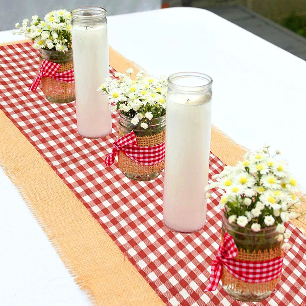 A display of white candles and small floral arrangements set on a red and white checkered table runner.