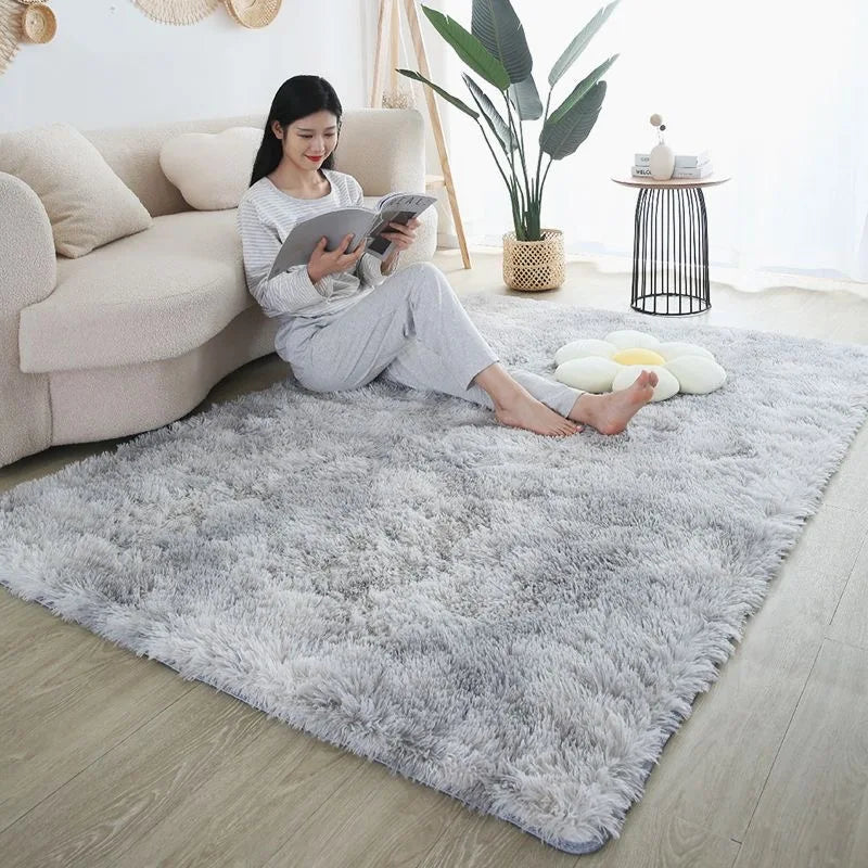 A fluffy gray rug is placed on a light wood floor in a bright room with a sofa and potted plant.