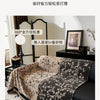 A black chenille sofa slipcover draped over a dark leather sofa, featuring a floral pattern.